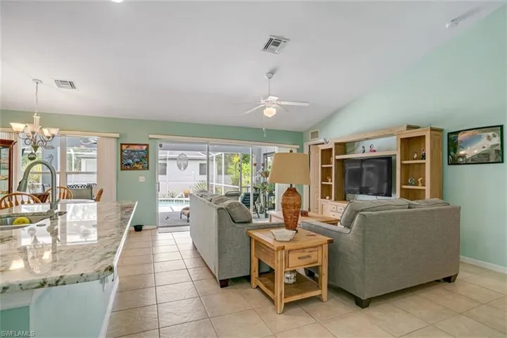 Living room with sink, vaulted ceiling, light tile floors, and ceiling fan with notable chandelier