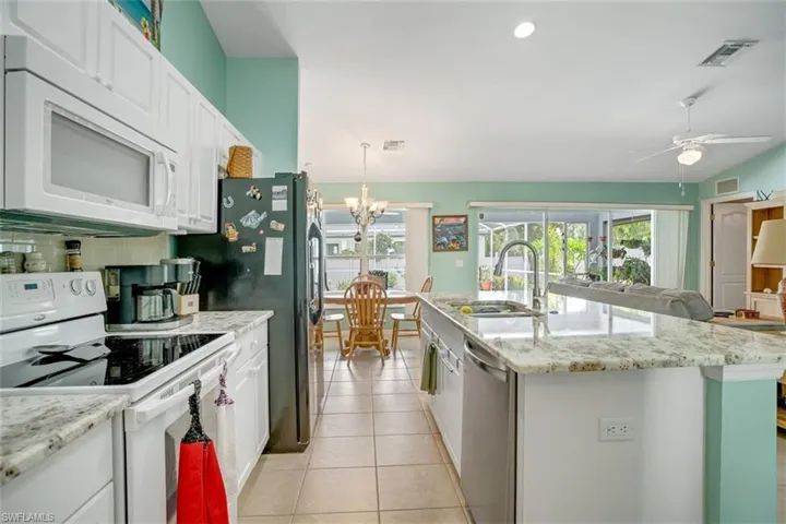 Kitchen with ceiling fan with notable chandelier, a center island with sink, white cabinetry, white appliances, and light tile floors