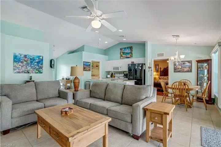 Tiled living room featuring high vaulted ceiling and ceiling fan with notable chandelier