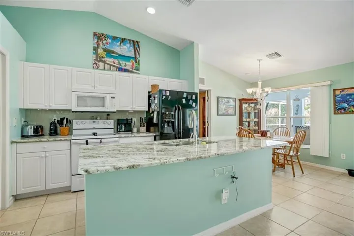 Kitchen featuring hanging light fixtures, a center island with sink, vaulted ceiling, and white appliances
