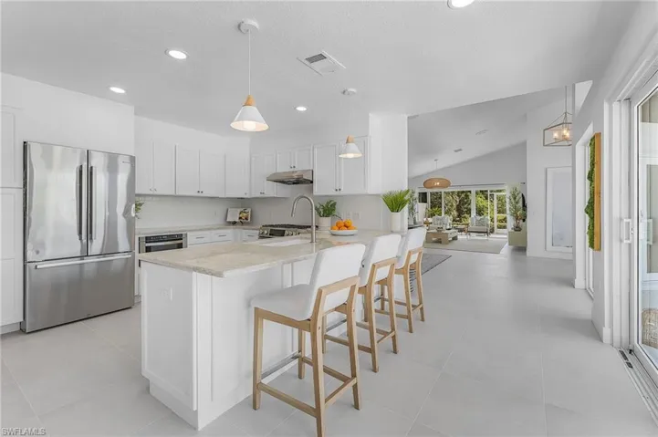 Kitchen featuring a kitchen breakfast bar, lofted ceiling, stainless steel appliances, decorative light fixtures, and light tile floors
