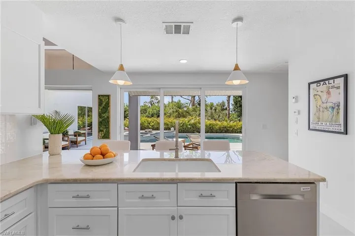 Kitchen featuring decorative light fixtures, white cabinets, dishwasher, and light stone countertops