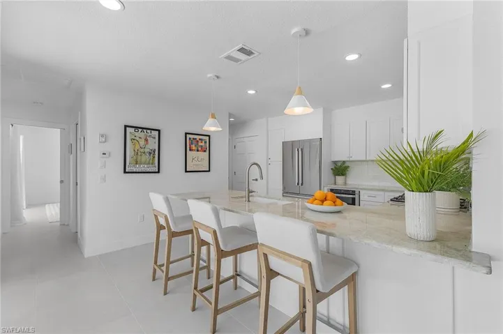 Kitchen featuring high end refrigerator, decorative light fixtures, sink, a breakfast bar area, and white cabinetry