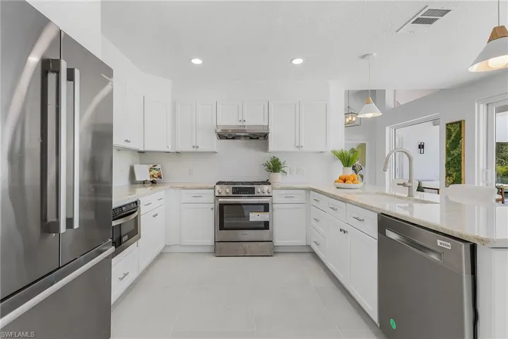 Kitchen with kitchen peninsula, stainless steel appliances, decorative light fixtures, light tile floors, and sink