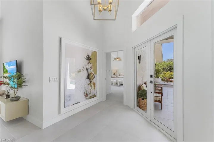 Hall with a towering ceiling, light tile floors, and an inviting chandelier