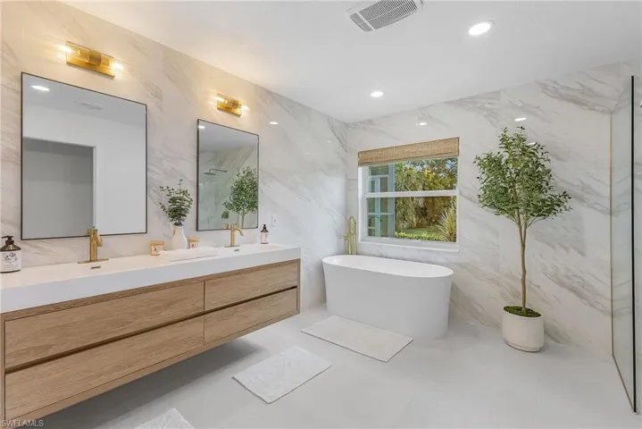 Bathroom with dual bowl vanity, tile flooring, tile walls, and a bath
