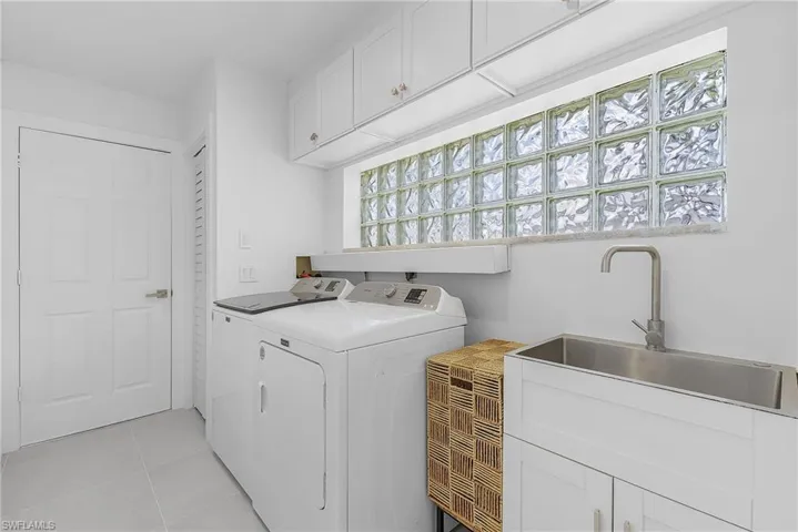Clothes washing area featuring cabinets, sink, washer and clothes dryer, and light tile floors