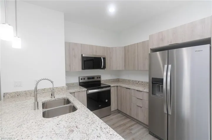 Kitchen with stainless steel appliances, light brown cabinets, a sink, and light stone counters