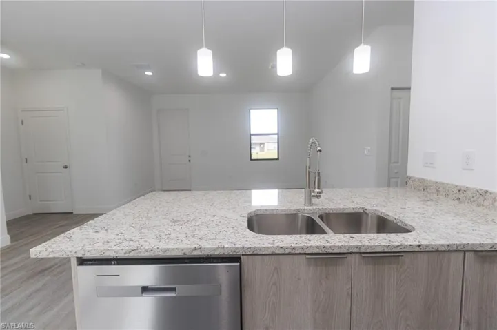 Kitchen featuring light stone counters, light vinyl flooring, a sink, stainless steel dishwasher, and light brown cabinetry