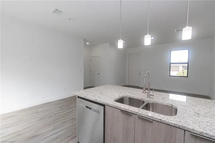 Kitchen with light vinyl flooring, decorative light fixtures, a sink, and stainless steel dishwasher