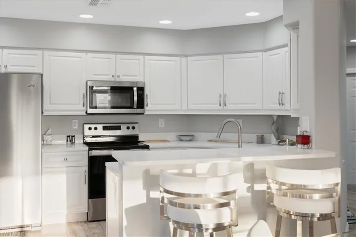 Kitchen with stainless steel appliances, a breakfast bar area, white cabinetry, a peninsula, and light wood-style floors