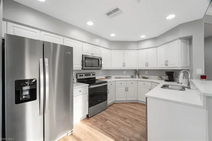 Kitchen with stainless steel appliances, white cabinets, recessed lighting, light wood finished floors, and light stone countertops