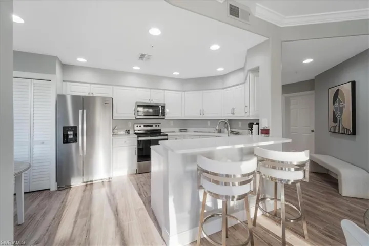 Kitchen featuring appliances with stainless steel finishes, a breakfast bar area, white cabinets, light wood-style floors, and recessed lighting