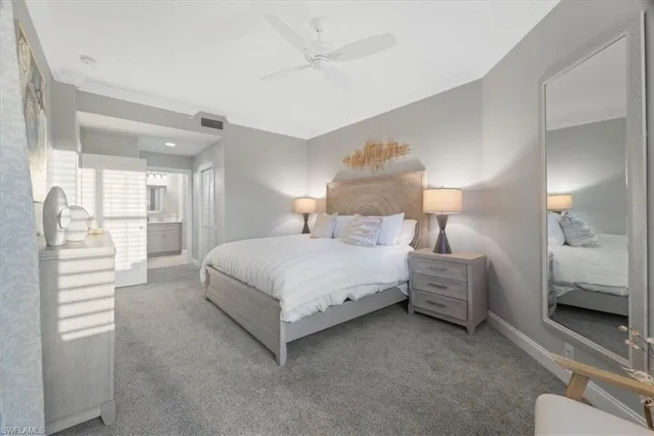 Carpeted bedroom with ensuite bathroom, ornamental molding, and ceiling fan