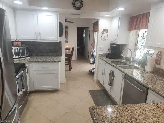 Kitchen with appliances with stainless steel finishes, white cabinets, tasteful backsplash, light tile patterned flooring, and recessed lighting
