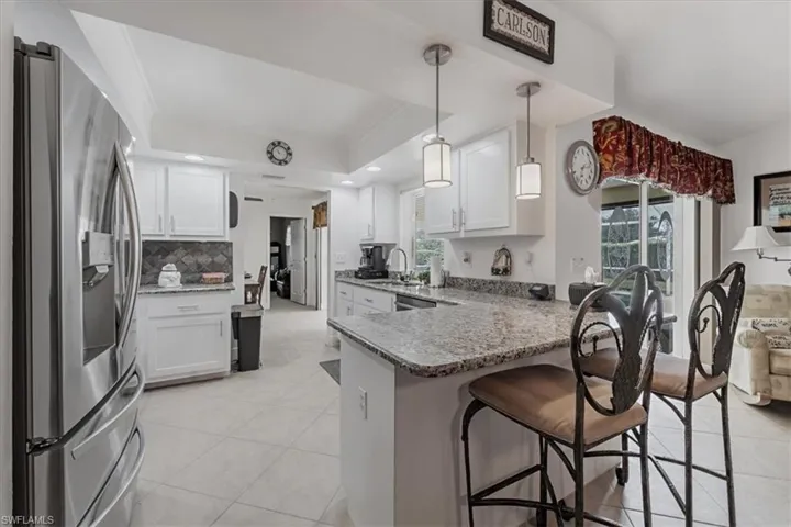 Kitchen with stainless steel refrigerator with ice dispenser, a peninsula, plenty of natural light, light stone countertops, and recessed lighting