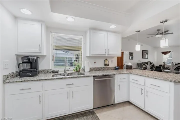 Kitchen featuring dishwasher, a peninsula, white cabinets, crown molding, and light stone counters