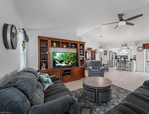 Living room featuring vaulted ceiling, a ceiling fan, and light tile patterned floors
