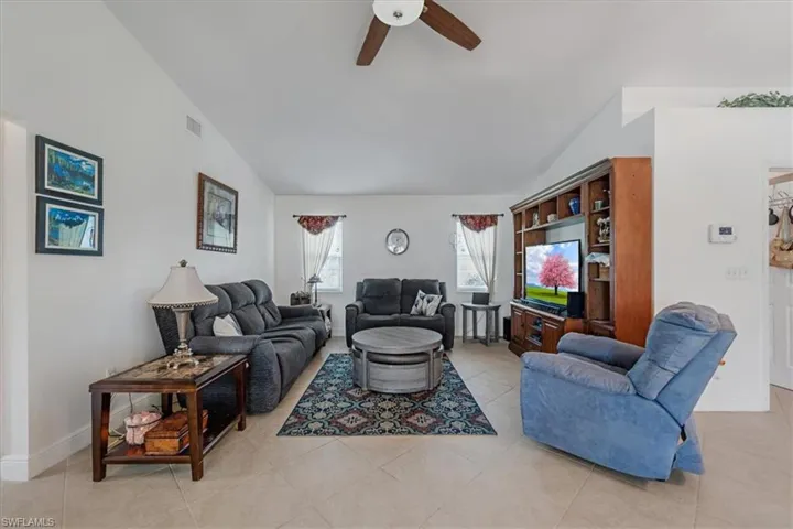 Living room featuring lofted ceiling, a ceiling fan, and light tile patterned flooring
