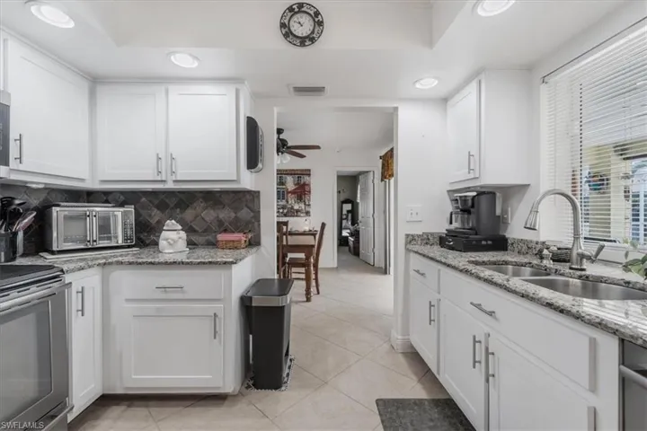 Kitchen featuring appliances with stainless steel finishes, white cabinets, light tile patterned floors, backsplash, and ceiling fan