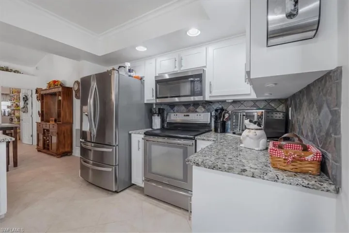 Kitchen featuring stainless steel appliances, white cabinetry, crown molding, tasteful backsplash, and light stone countertops