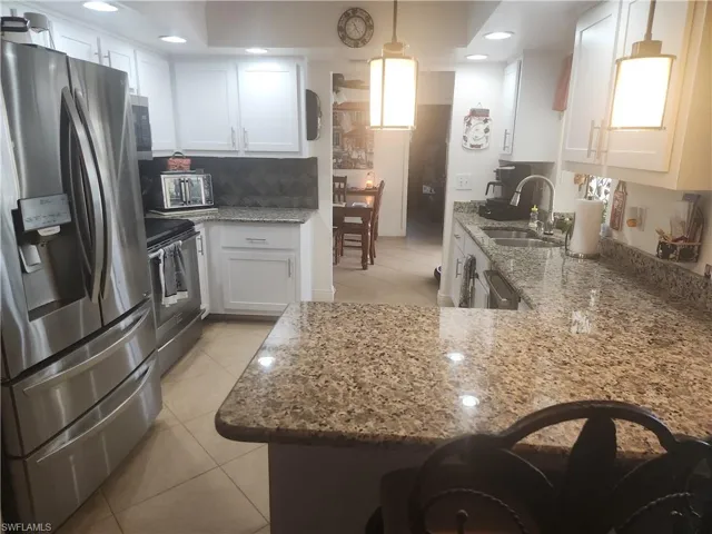 Kitchen with stainless steel appliances, light tile patterned flooring, white cabinets, light stone counters, and tasteful backsplash