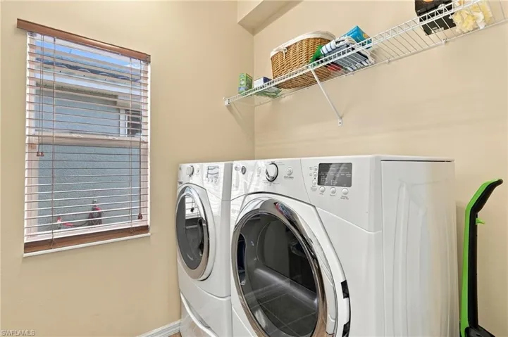 Laundry area featuring white front-load washer and dryer, window with wood-finish blinds, and metal wall-mounted shelving
