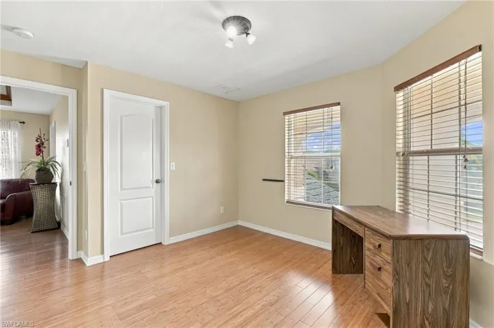 Neutral-toned room featuring wood-finish flooring, two large windows with integrated blinds, and a multi-panel interior door