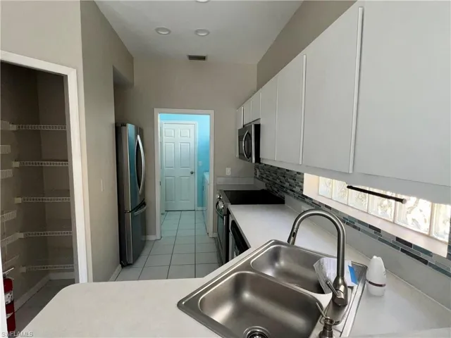 Kitchen featuring light countertops, white cabinets, stainless steel appliances, light tile patterned flooring, and decorative backsplash