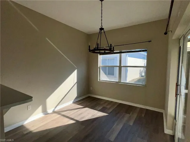 Unfurnished dining area with hanging lights and dark wood finished floors