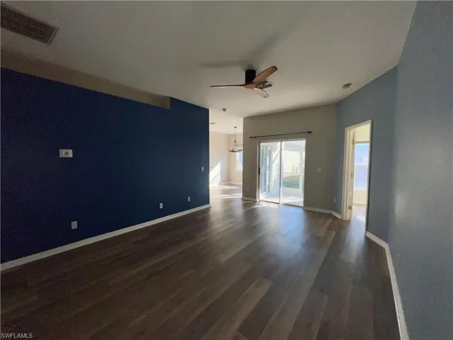 Empty room with ceiling fan, dark wood-type flooring, and hanging lights