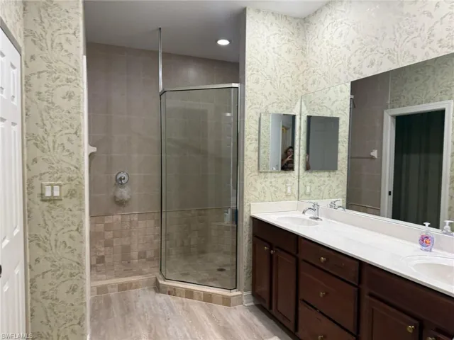Full bathroom featuring wallpapered walls, a shower stall, double vanity, and light wood finished floors