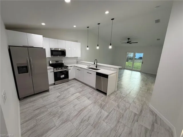 Kitchen featuring stainless steel appliances, white cabinetry, hanging light fixtures, light countertops, and lofted ceiling