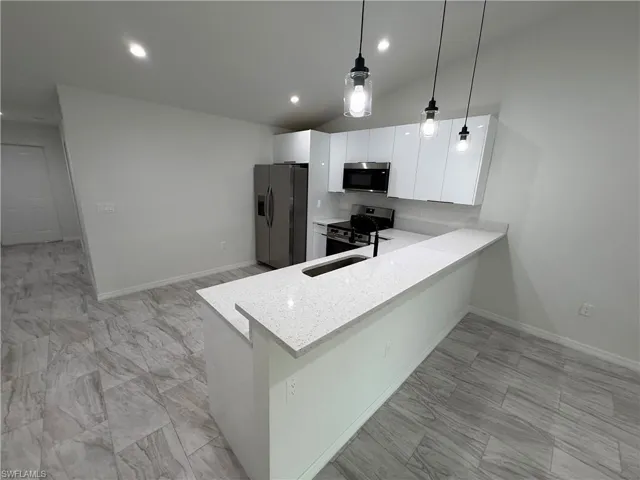 Kitchen featuring light stone countertops, a peninsula, decorative light fixtures, stainless steel appliances, and white cabinetry