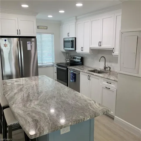 Kitchen featuring stainless steel appliances, white cabinetry, light stone counters, electric panel, and a center island
