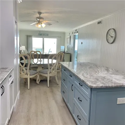 Kitchen with light stone countertops, light wood finished floors, a kitchen island, a ceiling fan, and crown molding