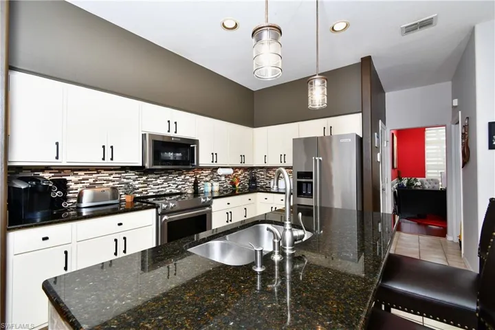 Kitchen featuring backsplash, hanging light fixtures, a center island with sink, white cabinets, and high quality appliances