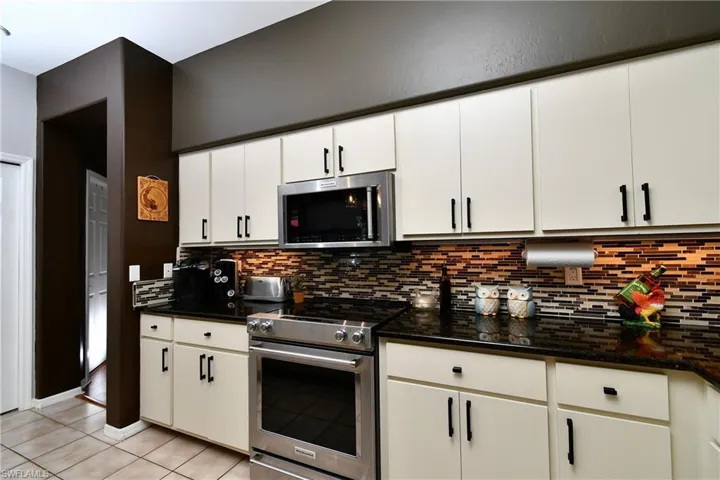Kitchen featuring qranite counters, tasteful backsplash, stainless steel appliances, light tile floors, and white cabinetry