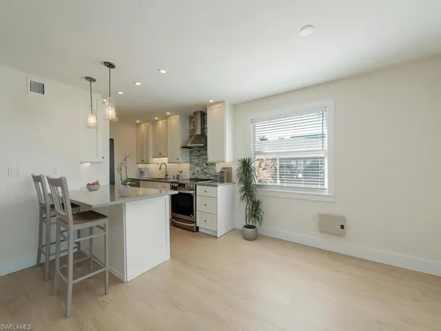 Virtually Staged Kitchen with a kitchen bar, decorative light fixtures, stainless steel range with electric cooktop, light wood style tile flooring, and a peninsula
