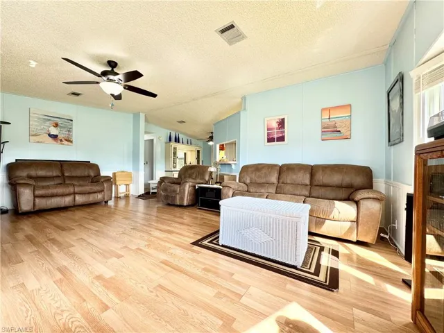 Living area with a textured ceiling, light wood-style flooring, visible vents, and a ceiling fan