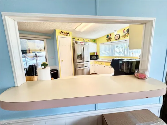 Kitchen with a textured ceiling, light countertops, stainless steel fridge, a peninsula, and black microwave