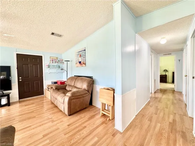 Living area featuring lofted ceiling, a textured ceiling, visible vents, and light wood finished floors