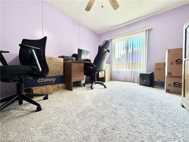 Carpeted home office featuring a ceiling fan, lofted ceiling, and a textured ceiling