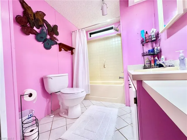 Bathroom with a textured ceiling, toilet, tile patterned floors, vanity, and shower / bath combo with shower curtain