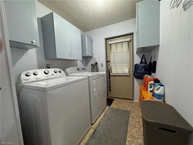 Laundry room featuring washing machine and clothes dryer, cabinet space, light floors, and a textured ceiling