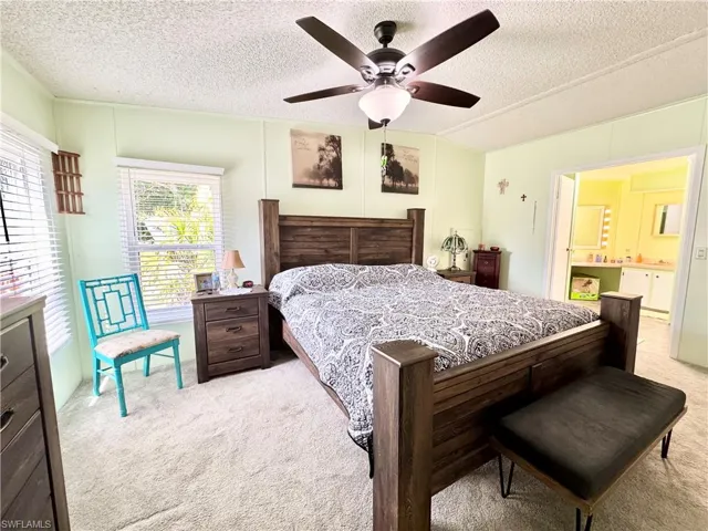 Bedroom featuring light carpet, ceiling fan, ensuite bathroom, and a textured ceiling