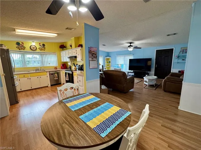 Dining space featuring light wood-type flooring, wainscoting, visible vents, and ceiling fan
