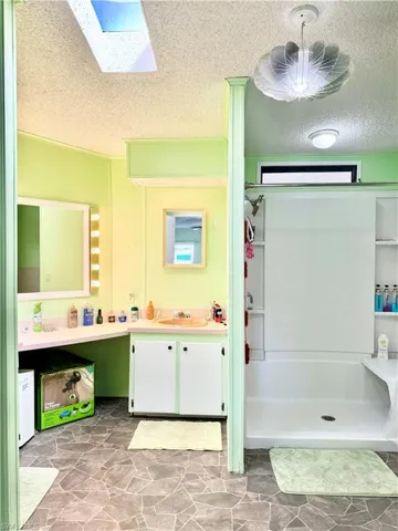 Full bathroom with a shower, vanity, a skylight, and a textured ceiling