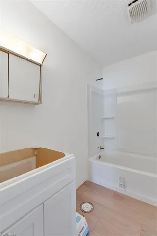 Bathroom featuring vanity, a textured ceiling, wood-type flooring, and tub / shower combination