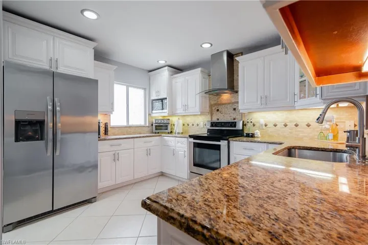 Kitchen featuring wall chimney exhaust hood, appliances with stainless steel finishes, and white cabinets